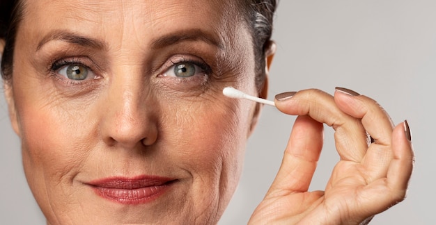 Free Photo elder woman with make-up on using cotton swab to remove it