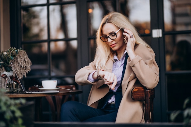 Free photo elderly businesswoman talking on phone and sitting outside the cafe