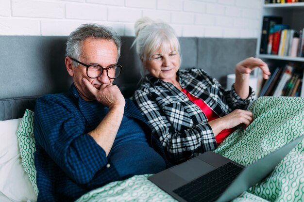 Elderly couple in bed looking at laptop