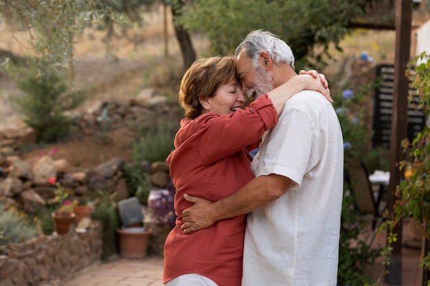 Elderly couple holding each other romantically at their countryside home garden