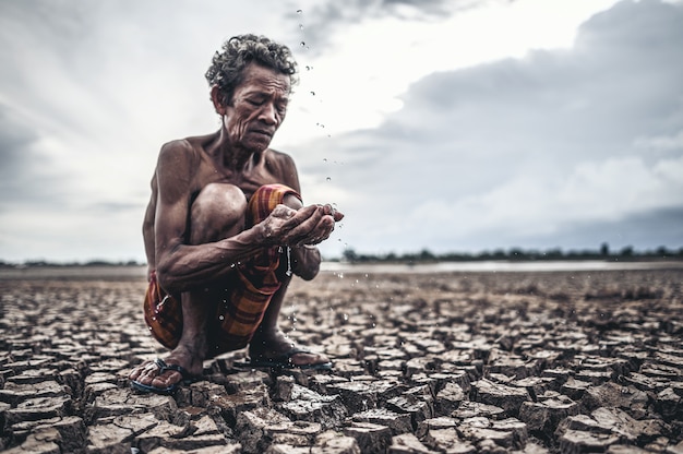 Free photo an elderly man sitting in touch with rain in the dry season, global warming, selection focus