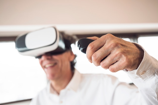 Free photo an elderly man wearing virtual reality goggles using remote control