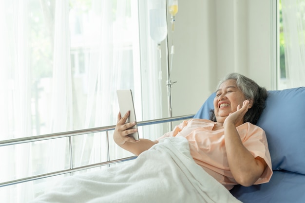 Elderly senior woman patients in hospital bed patients using smart phone call to descendant relatives feel happiness - senior female medical and healthcare concept