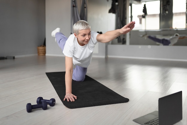 Free photo elderly woman doing yoga on a yoga mat at the gym