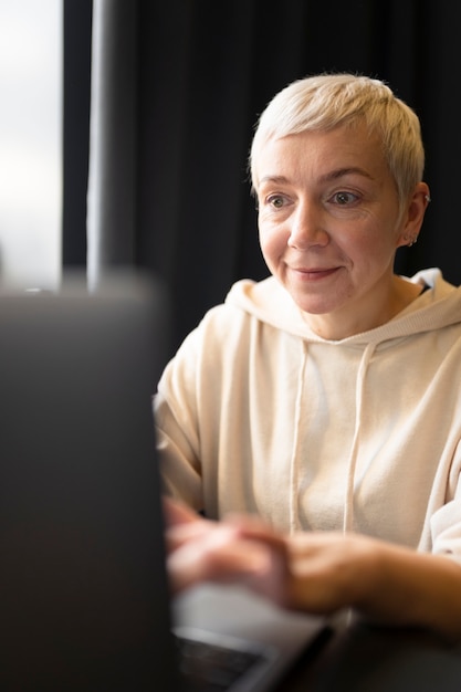 Elderly woman drinking coffee at a cafe while working on her laptop