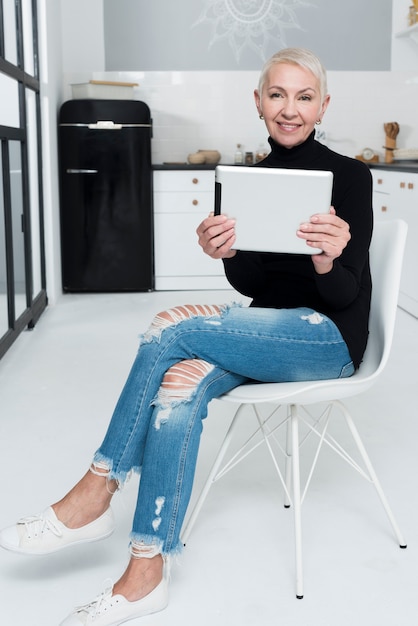 Elderly woman smiling and posing with tablet in the kitchen