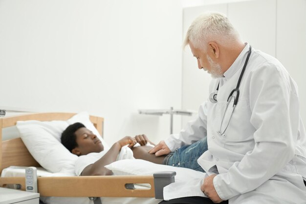 Eldery doctor examinating belly of african patient