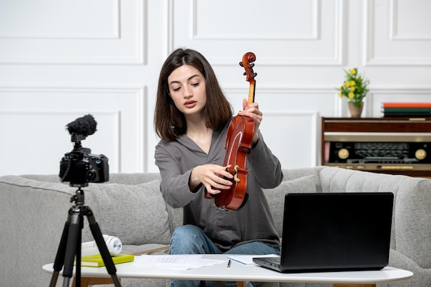 Elearning young cute beautiful girl remotely at home giving violin classes showing how to play