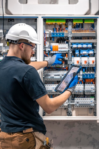 Free photo electrical technician working in a switchboard with fuses uses a tablet