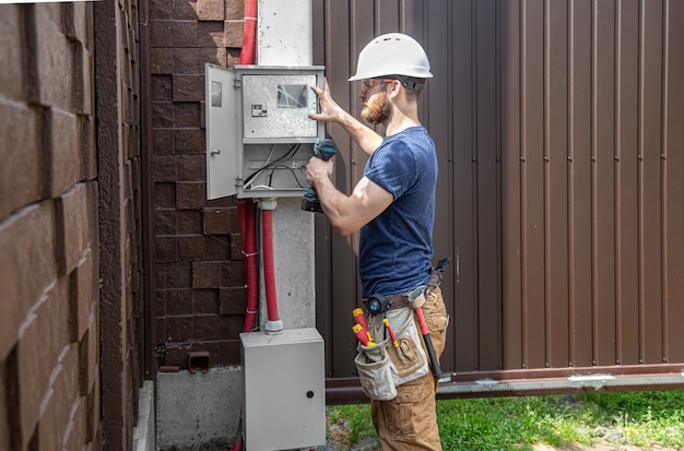 Electrician builder at work, examines the cable connection in the electrical line in the fuselage of an industrial switchboard. Professional in overalls with an electrician's tool.