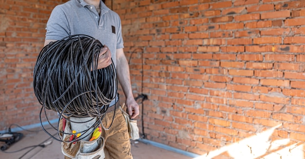 Free photo an electrician in a hard hat looks at the wall while holding an electric cable