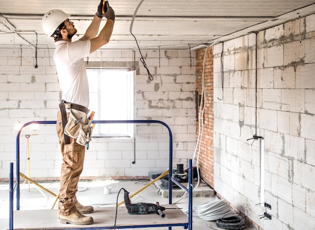 Electrician installer with a tool in his hands, working with cable on the construction site