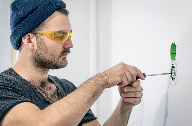 An electrician is mounting electric sockets on the white wall indoors