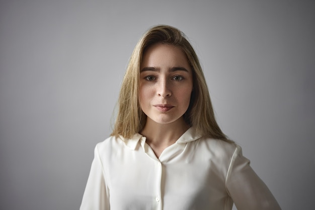 Elegance and glamour concept. Isolated image of fashionable glamourous neat young female with freckled face and loose blonde hair smiling joyfully, posing in studio wearing white silky blouse