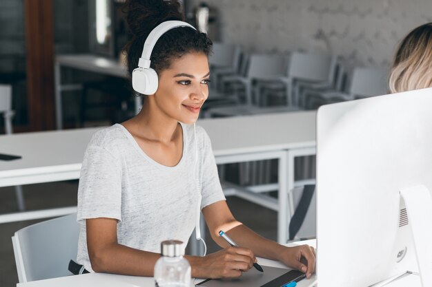 Free Photo elegant african web-designer doing her job in office with smile. attractive black woman in white headphones working in call-center, sitting near computer.