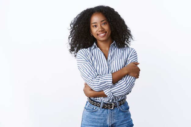 Elegant attractive tender feminine african american young woman curly-haired embracing herself showing female strong soft same time, smiling dreamy cuddling, wear collar shirt jeans white wall