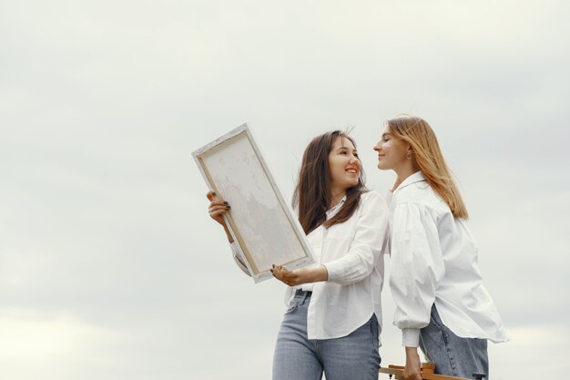 Elegant and beautiful girls painting in a field