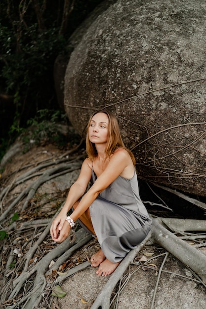 Elegant brunette woman in silk grey dress posing in on the rocks