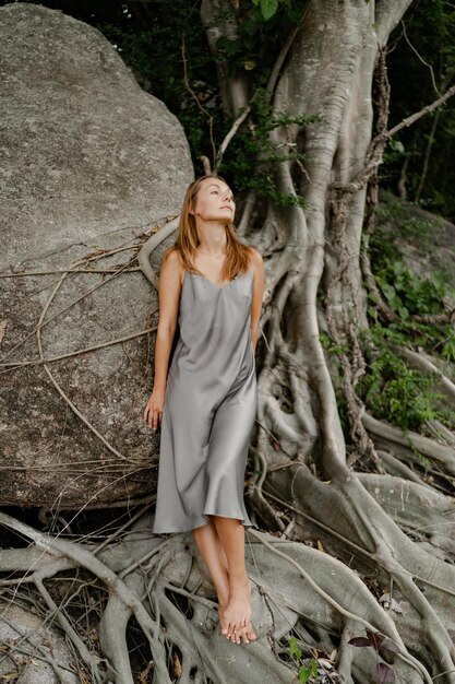 Elegant brunette woman in silk grey dress posing in on the rocks