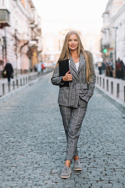 Elegant businesswoman walking in city with clipboard