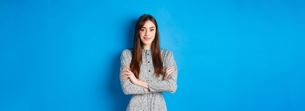 Free photo elegant caucasian girl in dress cross arms on chest standing on blue background