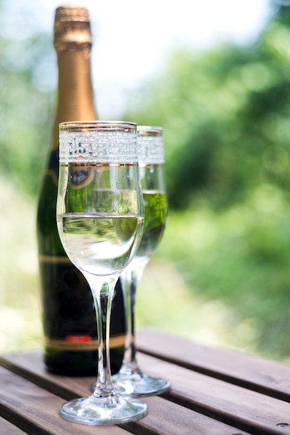 Elegant champagne glasses with champagne bottle on wooden table