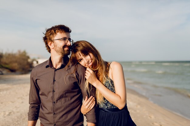 Elegant couple in love walking on sunny evening beach , happy woman embarrassing her husband.