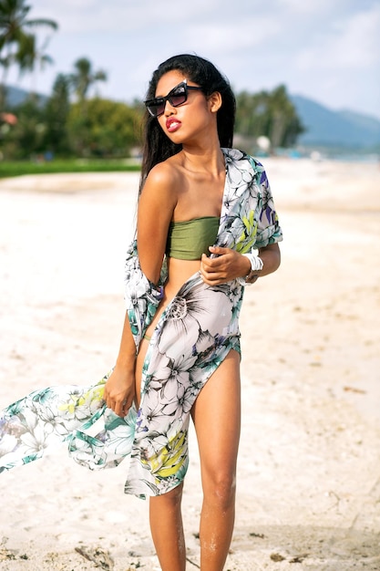 Free photo elegant fashionable woman posind at tropical exotic beach, luxury vacation, wearing bikini sunglasses and beachwear.