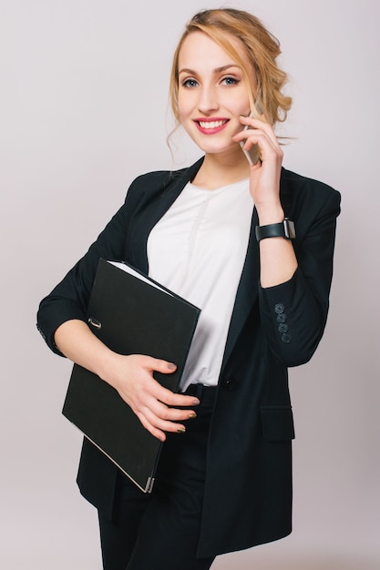 Free photo elegant fashionable young office woman in suit, holding folder, talking on phone isolated. cheerful mood, success, career, being busy, working, true positive emotions