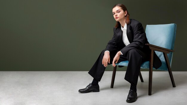 Elegant female model sitting in an armchair in a jacket suit. new feminity concept