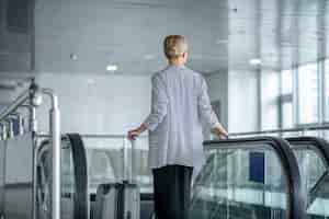 Free photo elegant female tourist with the trolley suitcase riding the escalator