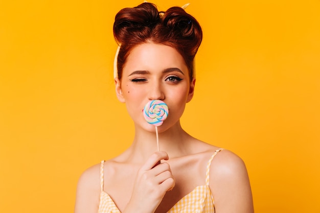 Elegant ginger girl licking lollipop. Front view of enthusiastic woman with hard candy.