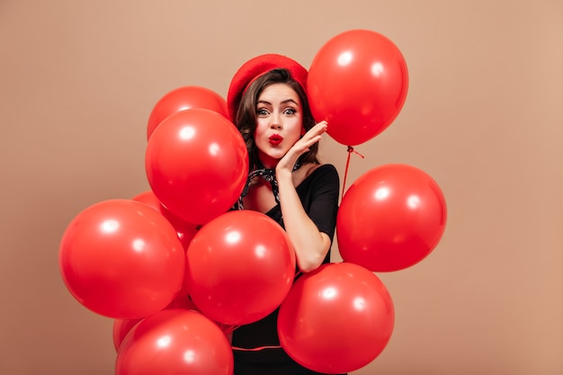 Free photo elegant girl in red beret and black dress blows kiss and holds huge balloons.