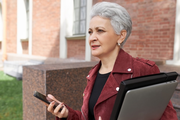 Elegant gray haired middle aged woman carrying laptop, going to business meeting, hurrying