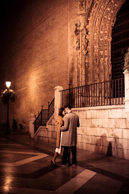 Free photo elegant lady hugging with young guy on street in evening