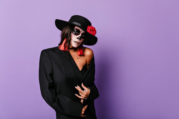 Free Photo elegant latin female model posing for halloween photoshoot. amazing young lady with spooky face painting standing on purple wall.