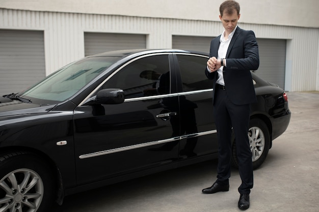 Elegant man standing next to his car for taxi services