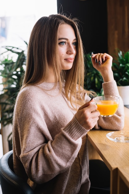 Elegant positive young woman holding cup of drink at bar counter in cafe