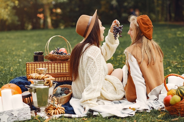 Free photo elegant and stylish girls sitting in a autumn park