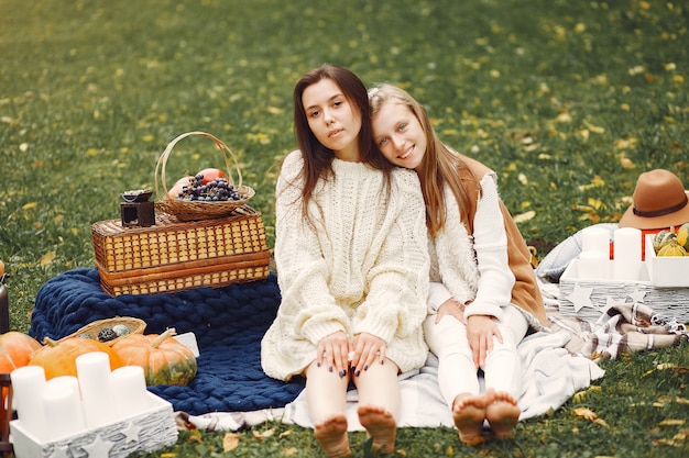 Free photo elegant and stylish girls sitting in a autumn park