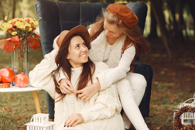 Free photo elegant and stylish girls sitting on a chair in a park