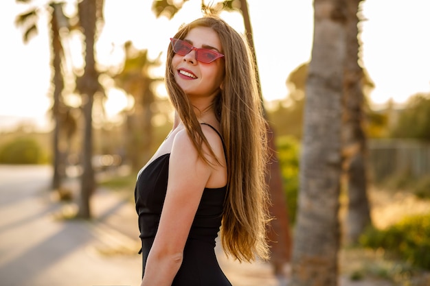 Elegant stylish woman posing near palms at sunset