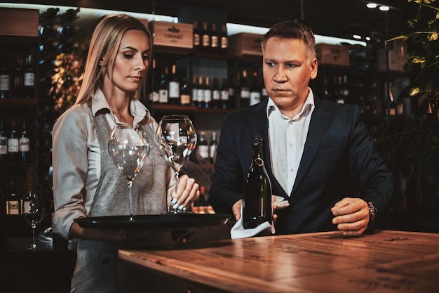 Elegant wine sommelier and his attractive assistant are ready to try new wine at private wine boutique.