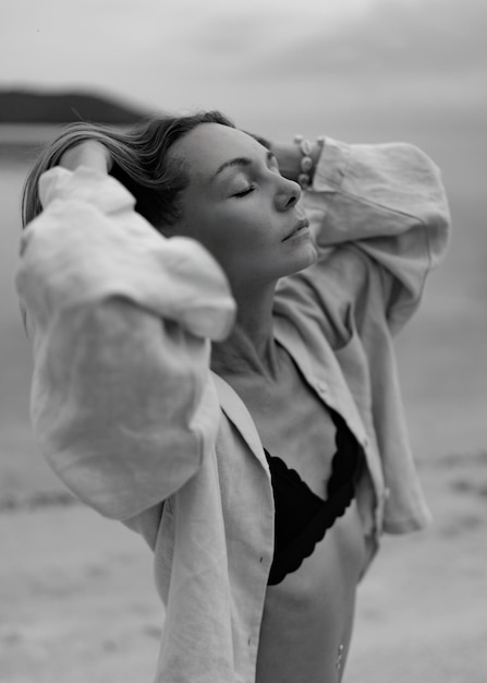 Elegant woman in casual outfit posing on lonely beach in cloudy weather Black and white