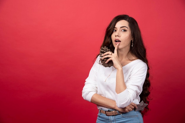 Elegant woman holding a big Christmas pinecone on red background. High quality photo