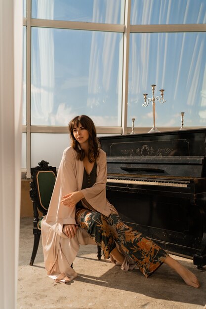 Elegant woman posing near piano in stylish light room.