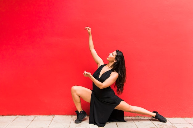 Free photo elegant young dancer dancing against red wall