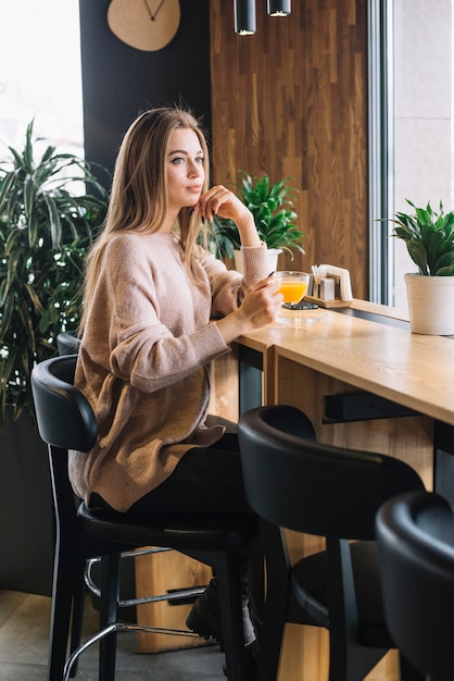 Elegant young thoughtful woman holding cup of drink at bar counter in cafe