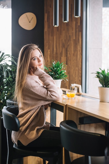 Free photo elegant young thoughtful woman with cup of drink at bar counter in cafe