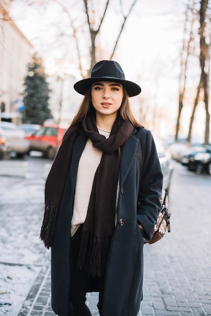 Free photo elegant young woman in hat and coat with scarf on street